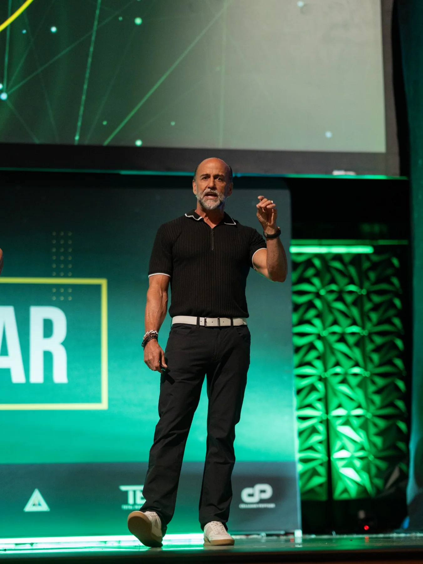 Executive speaker presenting on a green-lit conference stage with a clean, high-production look