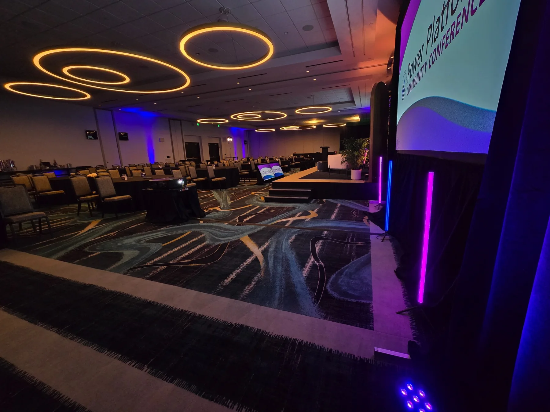 Modern breakout room with circular ceiling lights, stage steps, and blue-purple accent lighting