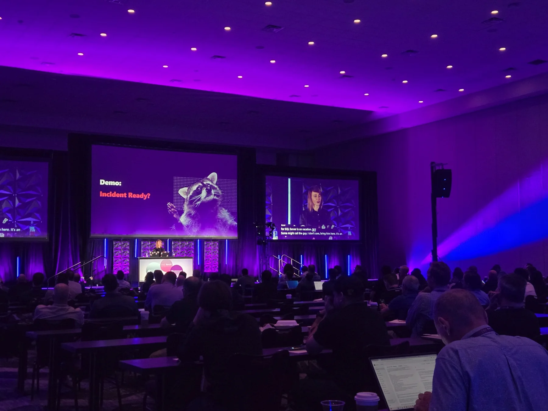 Wide corporate breakout room with purple lighting, audience seating, and large presentation screens