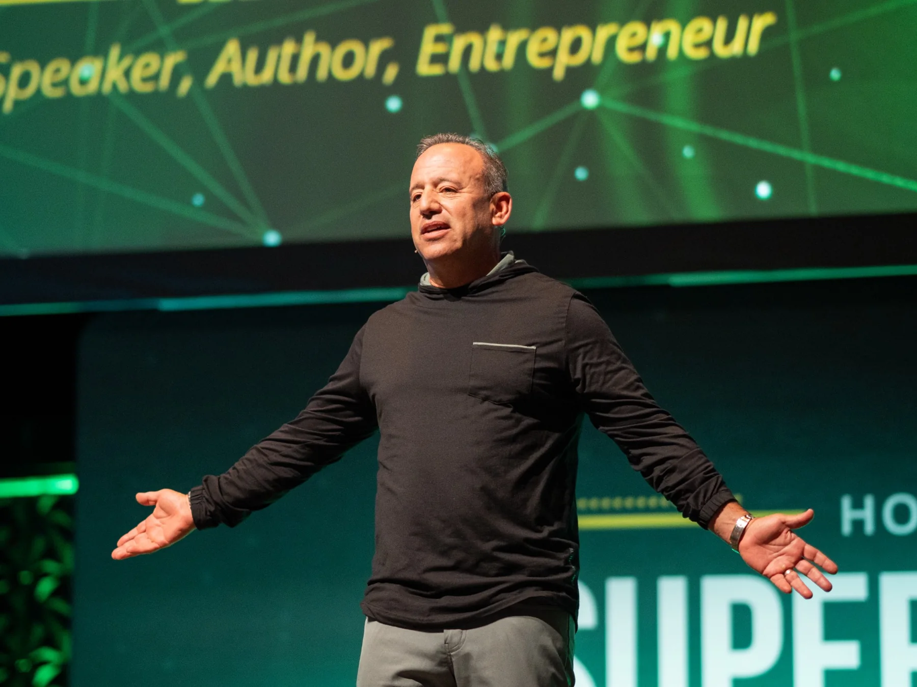 Corporate speaker on stage with face clearly visible, presenting in front of a green branded backdrop