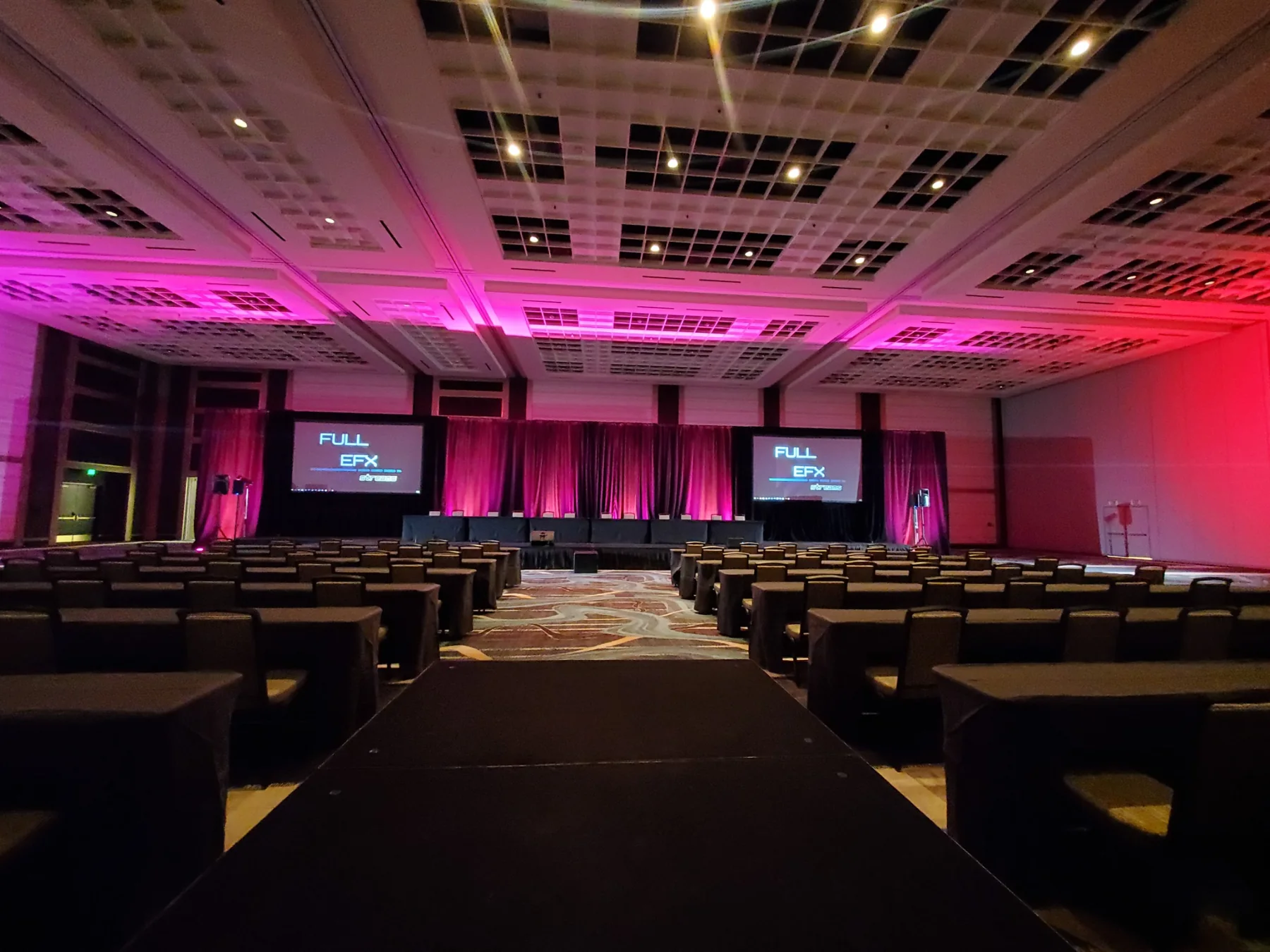Empty corporate ballroom prepared for a session with stage, screens, and magenta room lighting